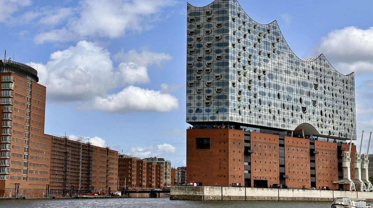 L'Elbphilharmonie de Hamburg reflétée dans les eaux calmes du port au lever du soleil, avec silhouette d'une grue portuaire historique symbolisant le dialogue entre tradition maritime et modernité.